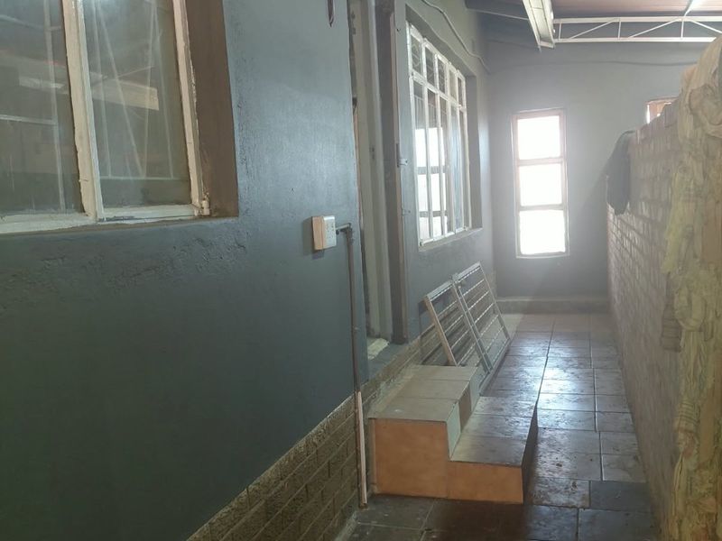 A covered outdoor walkway or patio area featuring tiled flooring, brick walling, and a metal roof structure, providing access to the side of the house.