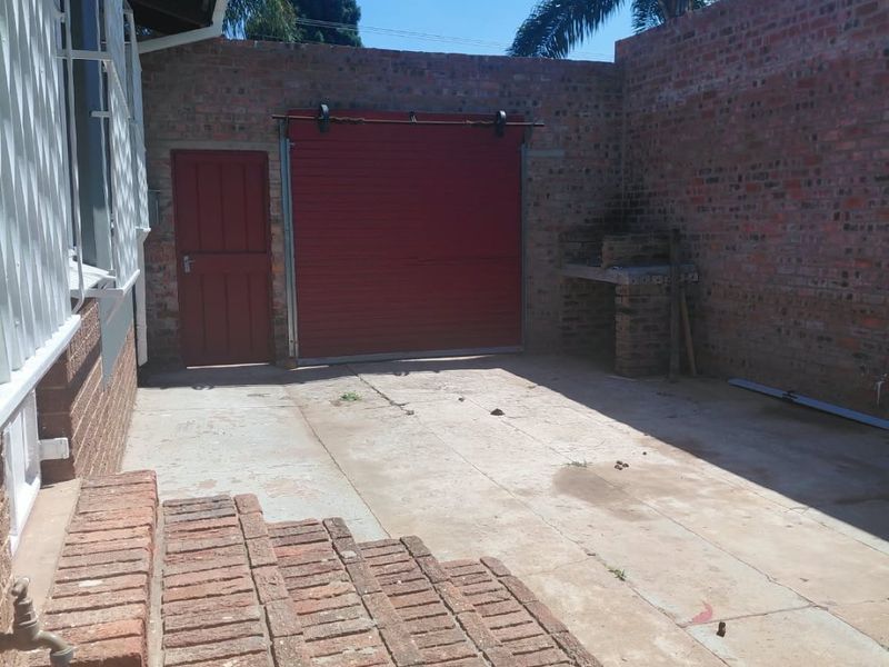 Rear courtyard area featuring a concrete patio, brick steps, built-in braai, and access to a garage and rear entrance.