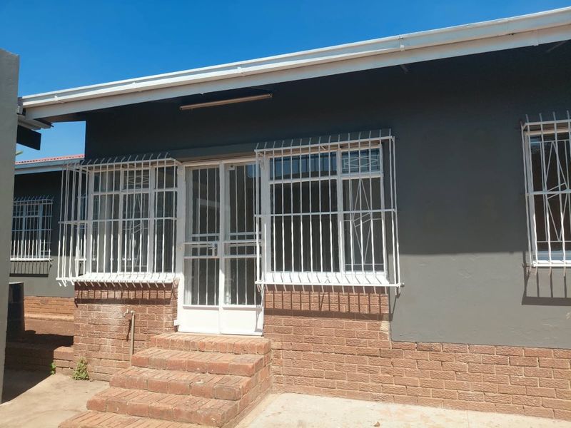Rear exterior view of the house featuring brick base, security bars on windows, and a security gate entrance with brick steps.