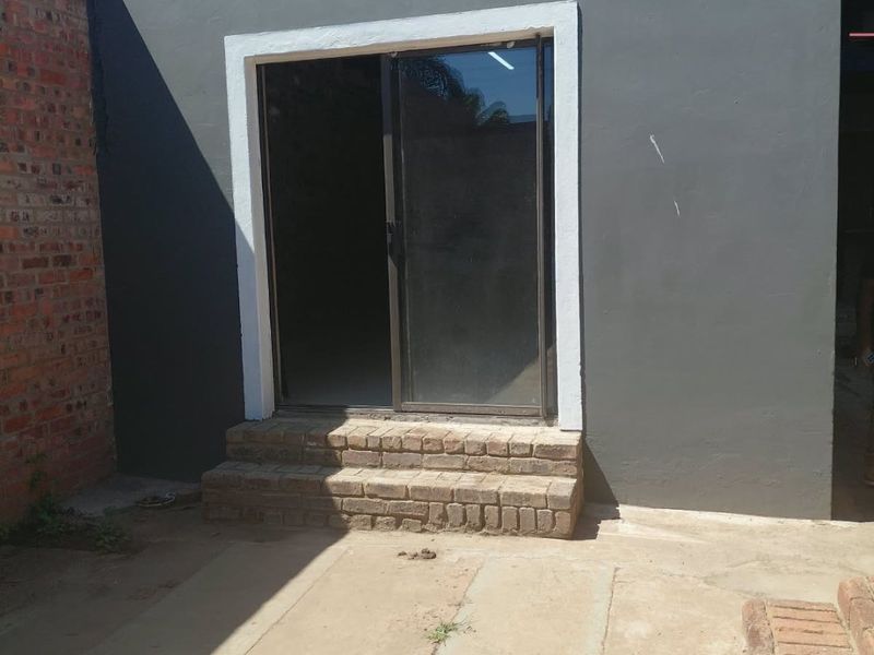 Rear exterior view showing a sliding glass door entrance with brick steps leading onto a concrete patio area.