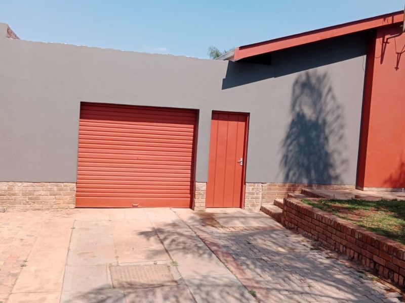 Front exterior view of the property featuring a roller garage door, pedestrian access door, and paved driveway with brick retaining wall elements.
