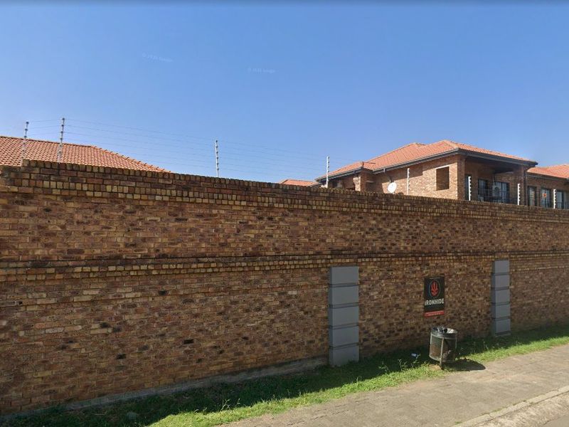 Street view of the property showing a secure brick boundary wall with electric fencing and tiled roof residential buildings in the background.