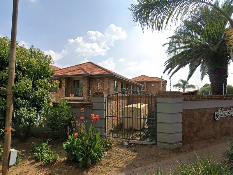 Street view of the apartment complex entrance featuring face brick construction, tiled roofing, and secure perimeter wall with electric fencing.