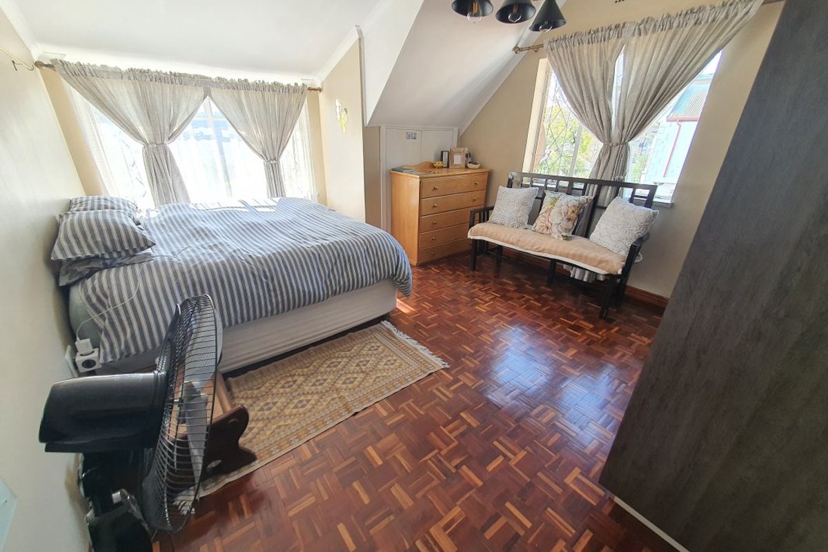 A spacious bedroom featuring classic parquet flooring, sloped ceilings, and natural light from dual windows.