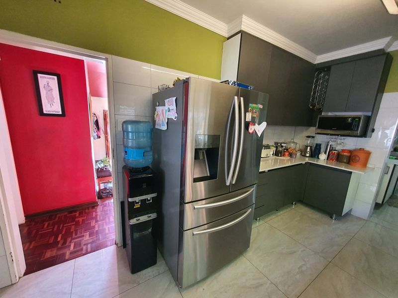 A functional kitchen featuring modern dark grey cabinetry, stone countertops, and a built-in microwave, complemented by neutral floor tiles and crown molding.