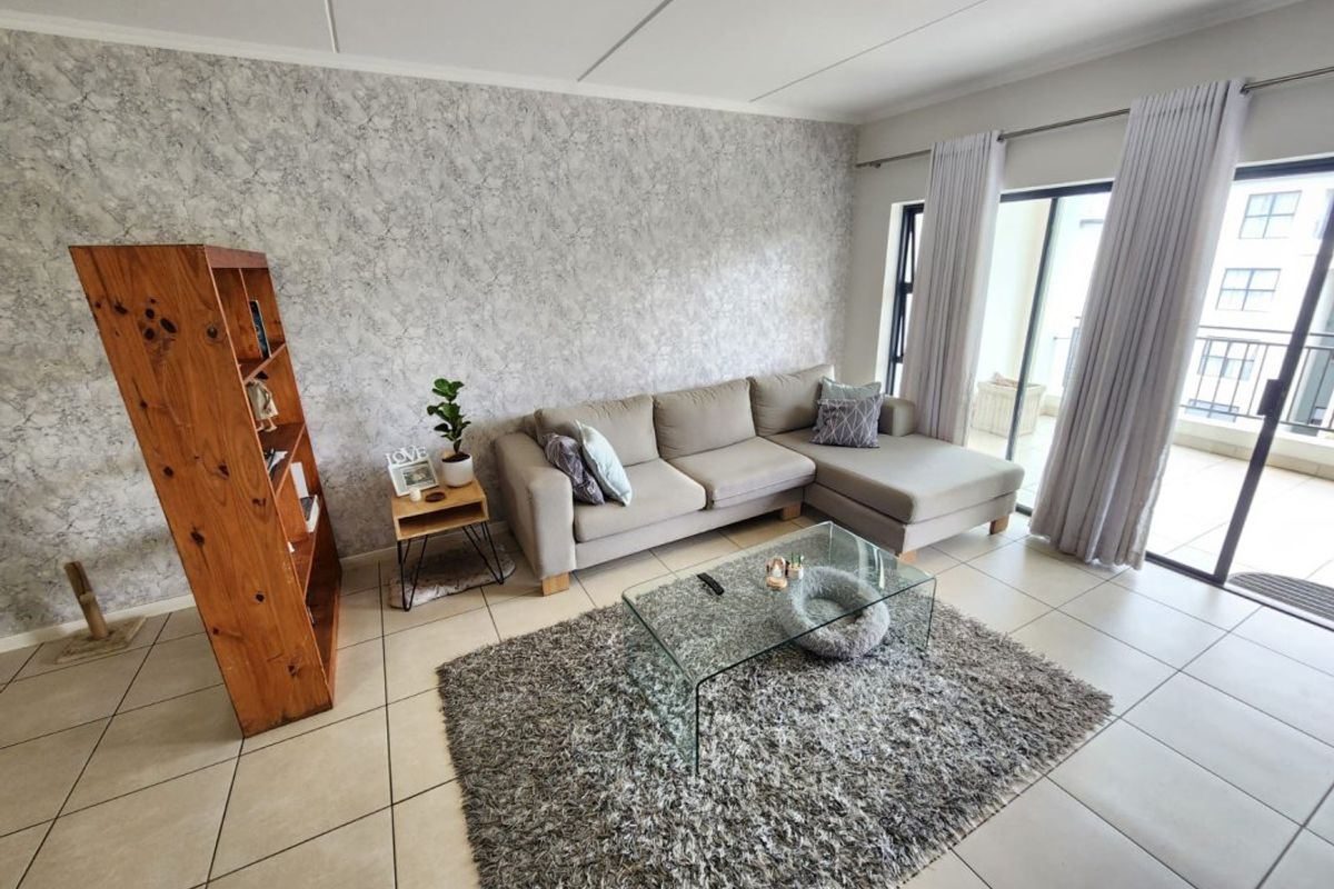 A bright living room featuring tiled flooring, a textured feature wall, and large sliding glass doors providing access to an outdoor balcony area.