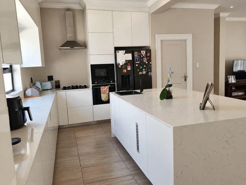 Modern kitchen featuring white cabinetry, quartz countertops, a central island with a sink, and integrated appliances, complemented by tiled flooring and crown molding.