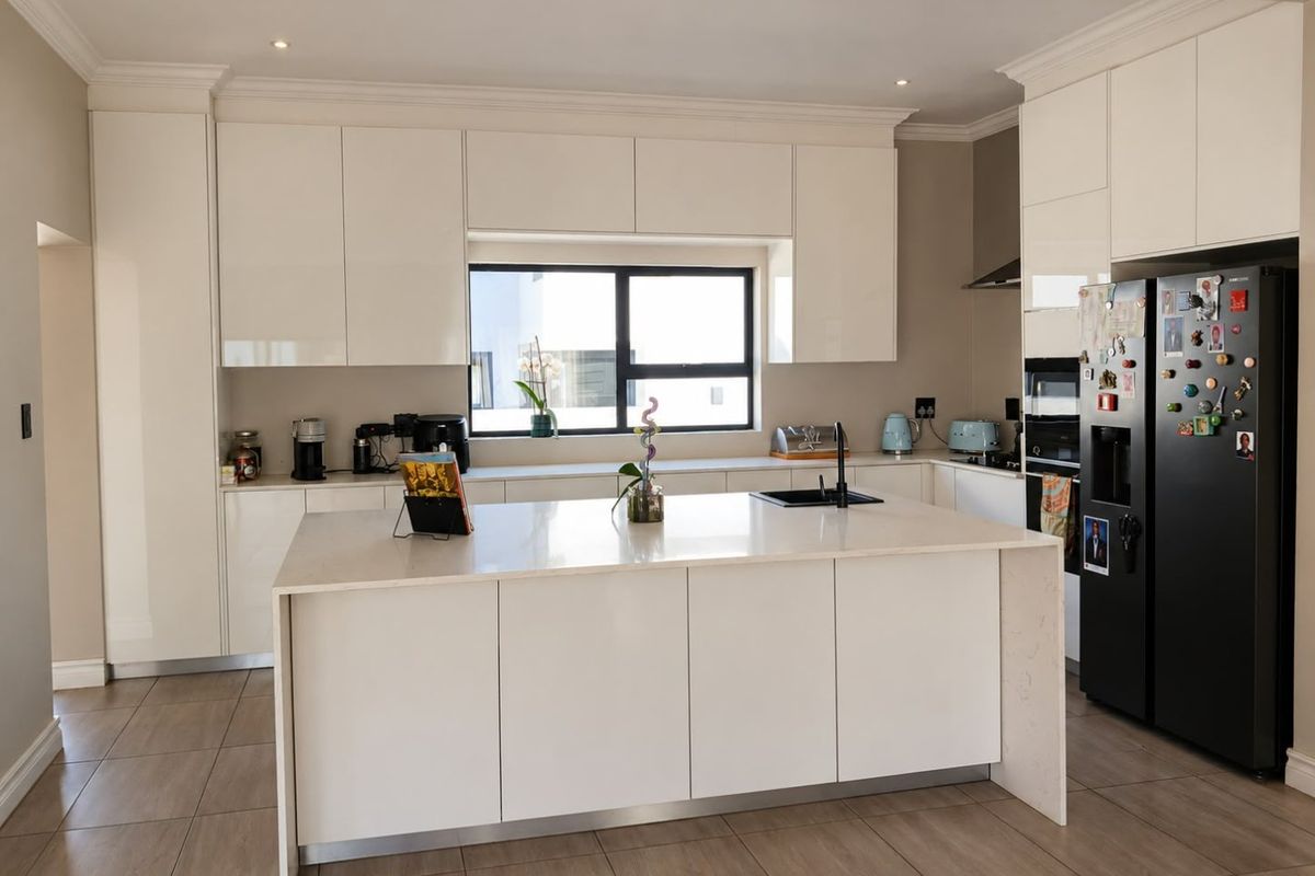Modern kitchen featuring sleek white cabinetry, a central island with quartz countertops, integrated appliances, and high-quality tiled flooring.