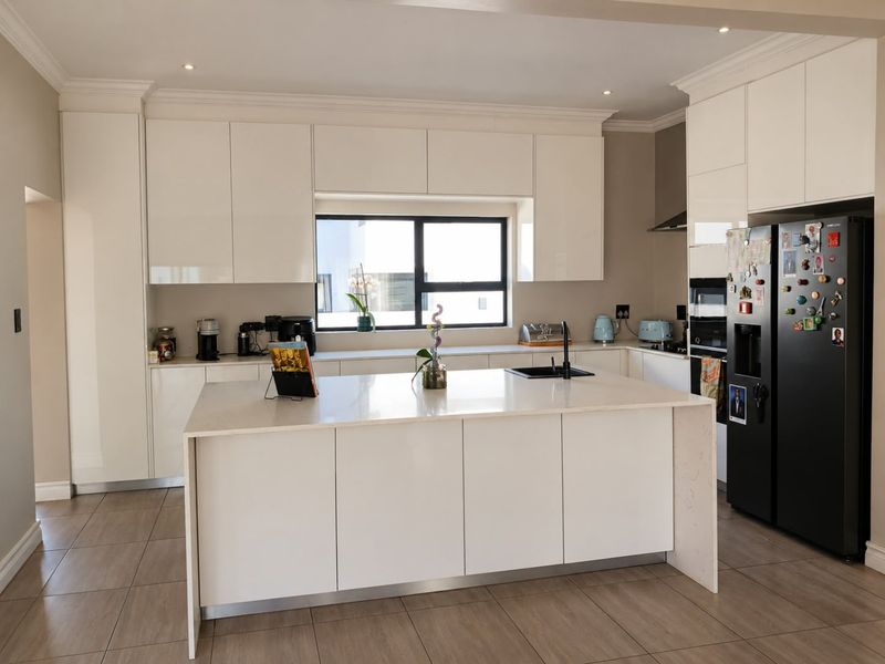 Modern kitchen featuring sleek white cabinetry, a central island with quartz countertops, integrated appliances, and high-quality tiled flooring.