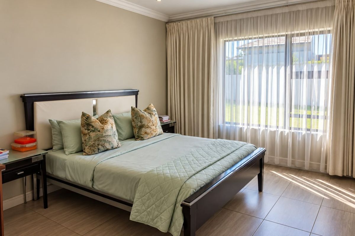 A well-maintained bedroom featuring neutral wall tones, tiled flooring, cove cornicing, and large windows with floor-to-ceiling curtains allowing for ample natural light.