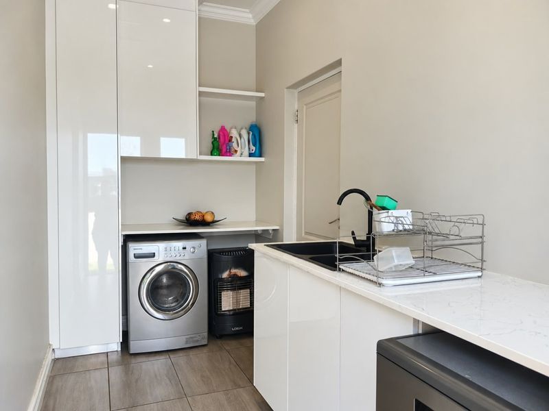 Modern laundry room featuring sleek white cabinetry, stone countertops, an undermount sink with a black mixer tap, and tiled flooring.