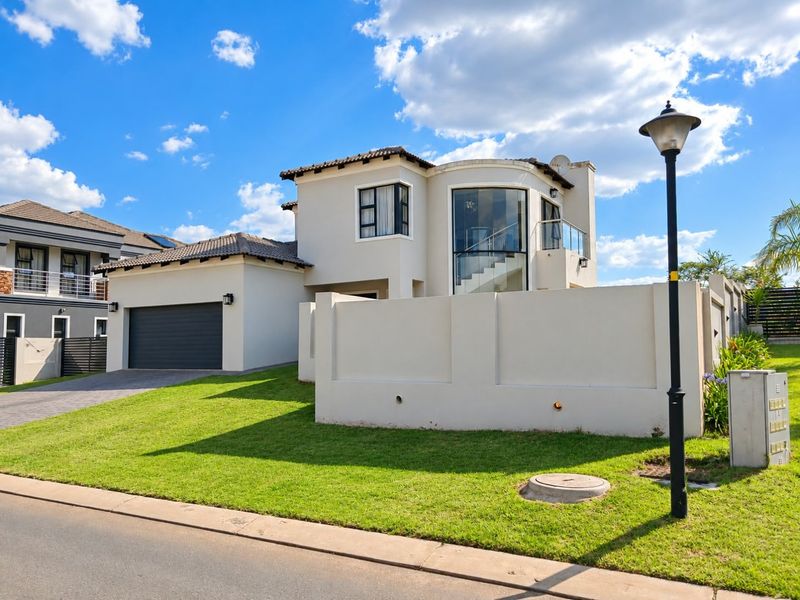 Modern double-story residential home featuring a paved driveway, double garage, and a distinctive curved glass facade with an upper-level balcony.