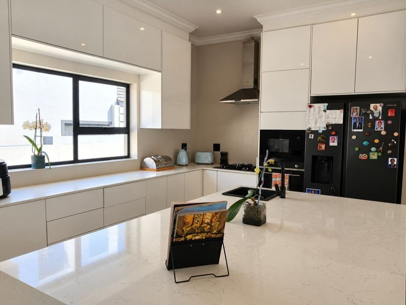 Modern kitchen featuring sleek white cabinetry, quartz countertops, a central island, and high-quality built-in appliances including a gas hob and extractor fan.