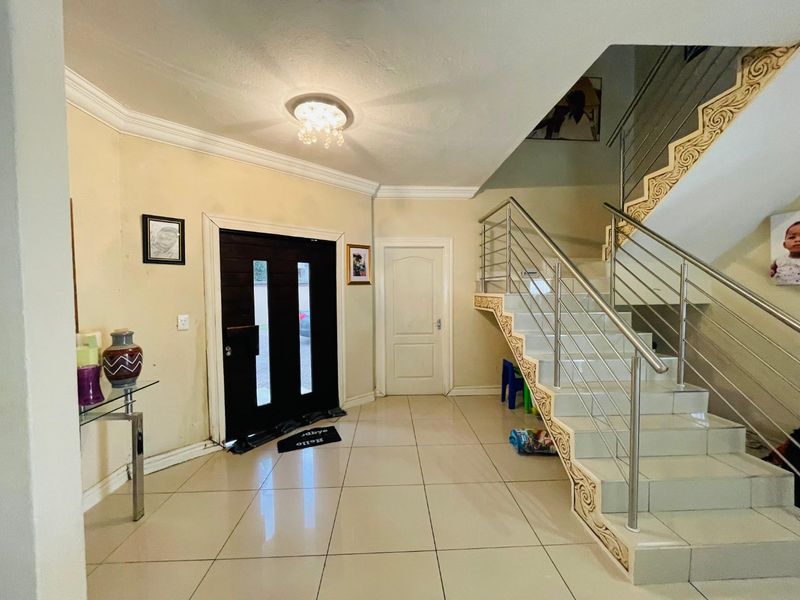 Spacious entrance hall featuring tiled flooring, a decorative staircase with stainless steel railings, and a modern front door with glass inserts.