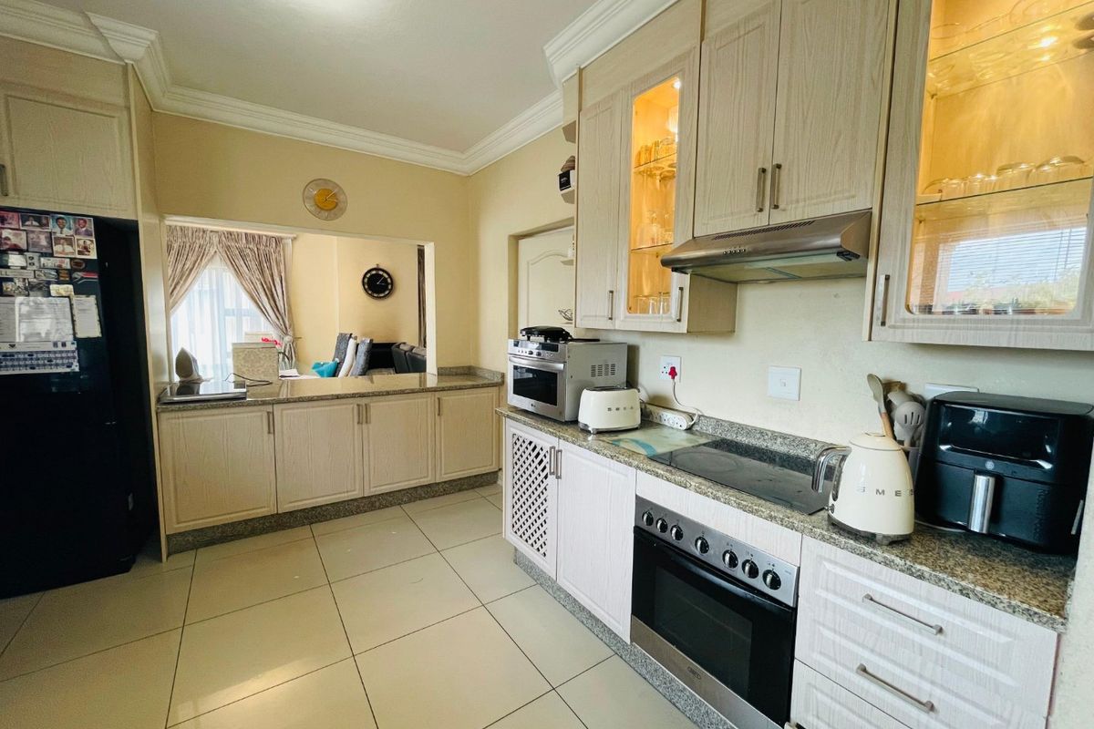 A functional kitchen featuring light wood cabinetry, granite countertops, built-in oven, and hob, with a convenient serving hatch opening into the adjacent living area.