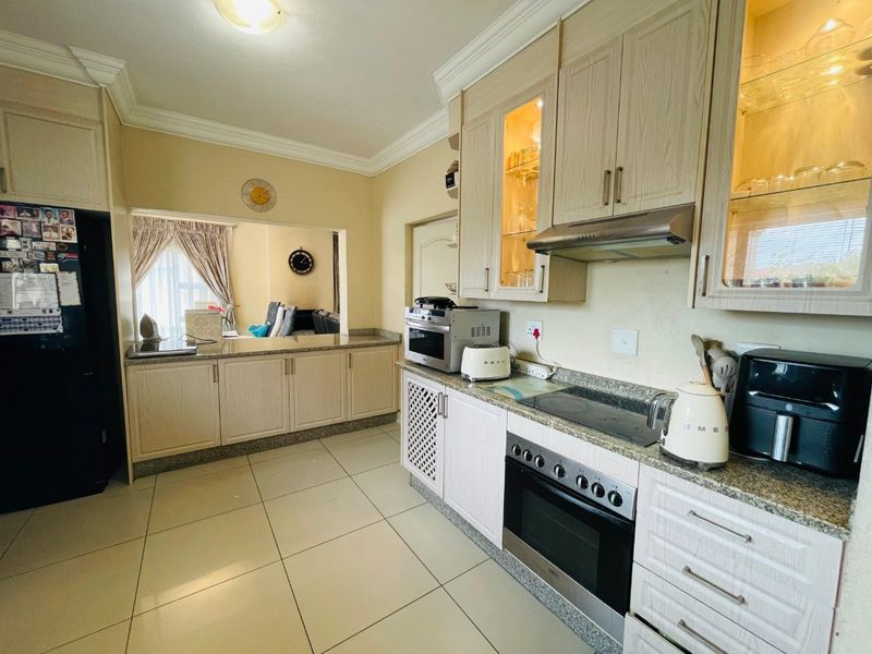 A functional kitchen featuring light wood cabinetry, granite countertops, built-in oven, and hob, with a convenient serving hatch opening into the adjacent living area.