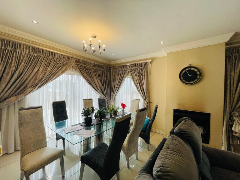 A well-lit dining area featuring tiled flooring, elegant cornicing, a built-in fireplace, and large windows dressed with floor-to-ceiling curtains.