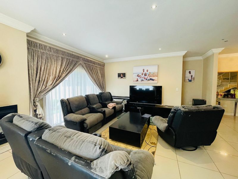 A spacious living room featuring tiled flooring, recessed downlighting, and large sliding glass doors with curtains, providing access to the exterior.
