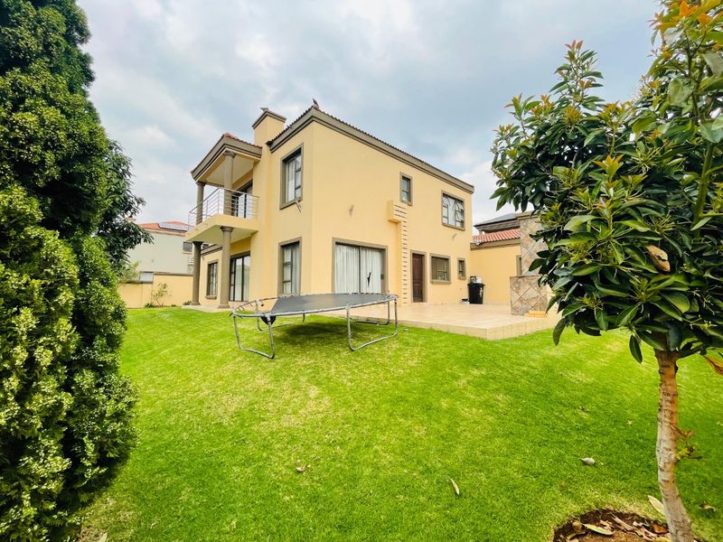 Rear view of a two-story house featuring a tiled patio, upper-level balcony, and a well-maintained lawn.