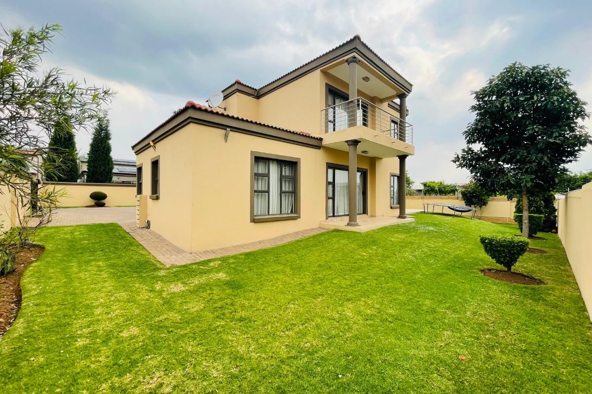 A well-maintained double-story residential property featuring a rear garden, paved walkways, and an upper-level balcony with metal railings.