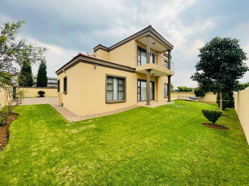 A well-maintained double-story residential property featuring a rear garden, paved walkways, and an upper-level balcony with metal railings.