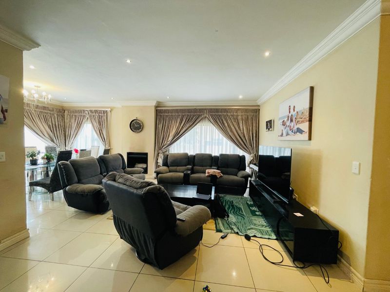 Spacious open-plan living and dining area featuring tiled flooring, recessed downlighting, crown molding, and a built-in fireplace.