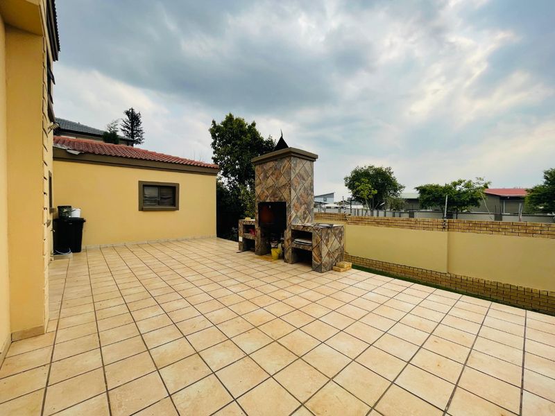 Spacious outdoor patio featuring a built-in braai area, tiled flooring, and secure brick boundary walls, ideal for outdoor entertaining.