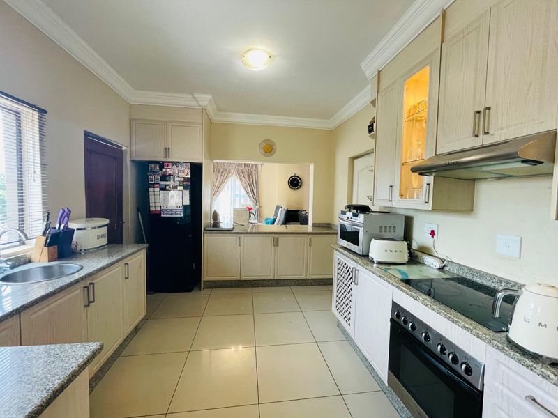 A functional kitchen featuring granite countertops, built-in cabinetry, an electric hob with extractor fan, and tiled flooring, offering a practical layout for daily use.