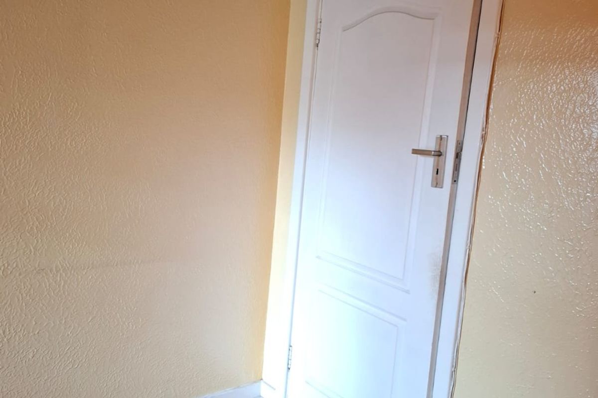 An empty bedroom featuring timber flooring and a standard internal door, requiring cosmetic updates to the wall finishes.