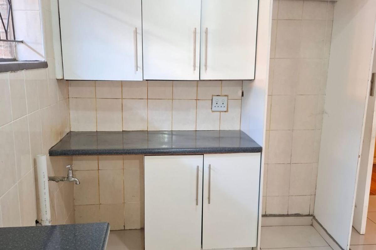A compact kitchen area featuring white built-in cabinetry, dark laminate countertops, and tiled finishes, currently vacant and ready for updates.