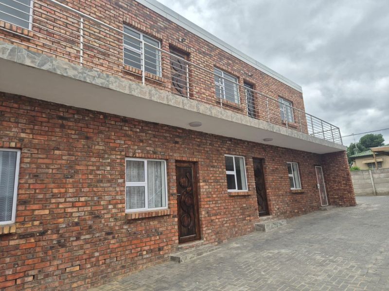 A two-story commercial building featuring a face brick facade, paved driveway, and an upper-level balcony with stainless steel balustrades.