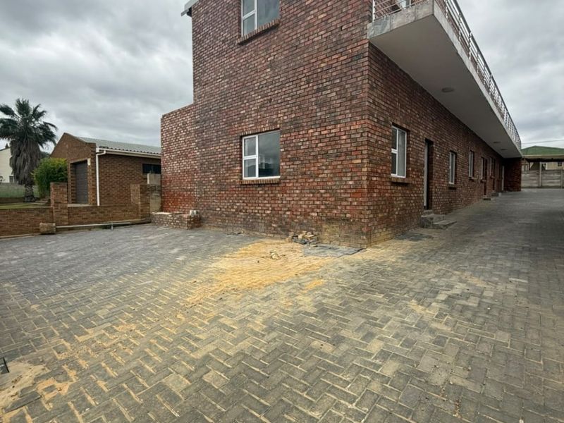 Rear view of a multi-story commercial face brick building featuring a paved driveway and an upper-level balcony with metal railings.