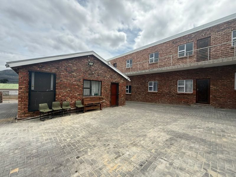 A paved commercial courtyard featuring face brick building facades, external security gates, and an upper-level balcony with metal railings.