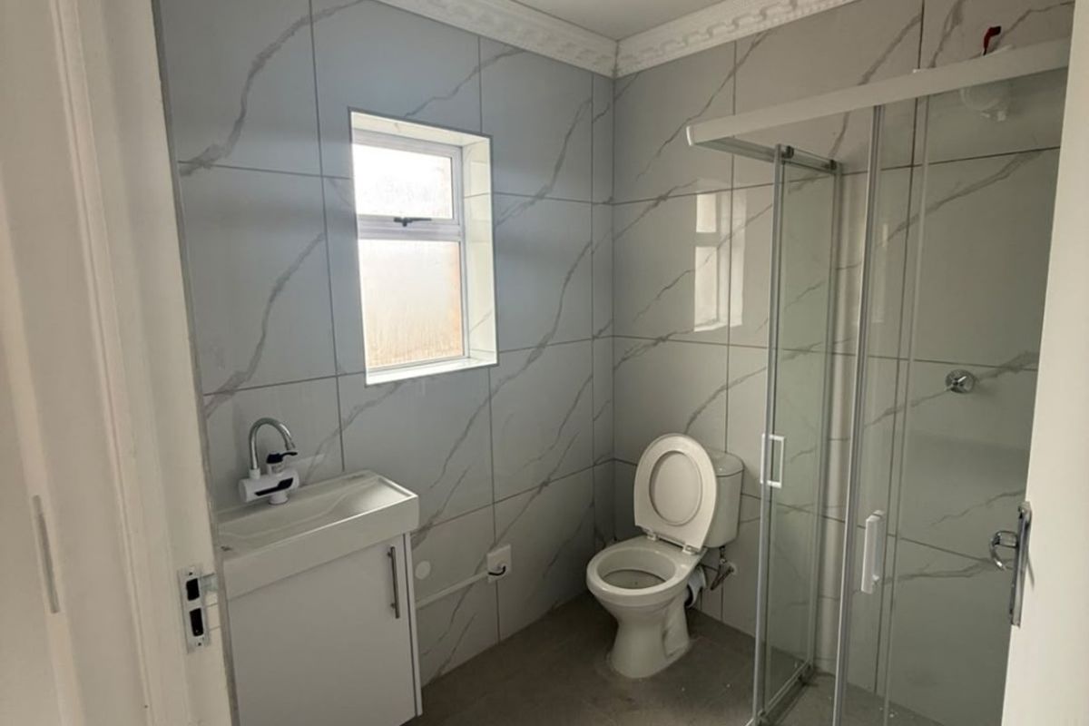 A compact bathroom featuring a shower enclosure, vanity basin, and toilet, finished with modern marble-look wall tiles and neutral floor tiles.