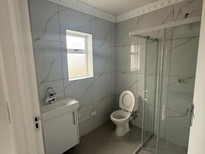 A compact bathroom featuring a shower enclosure, vanity basin, and toilet, finished with modern marble-look wall tiles and neutral floor tiles.