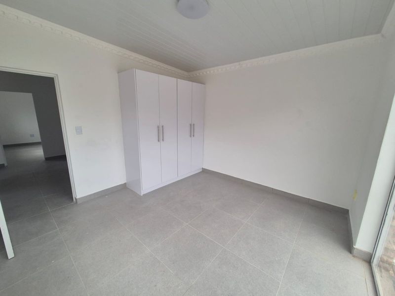 A clean, empty bedroom featuring neutral tiled flooring, a built-in wardrobe, and a classic tongue and groove ceiling with decorative cornice.
