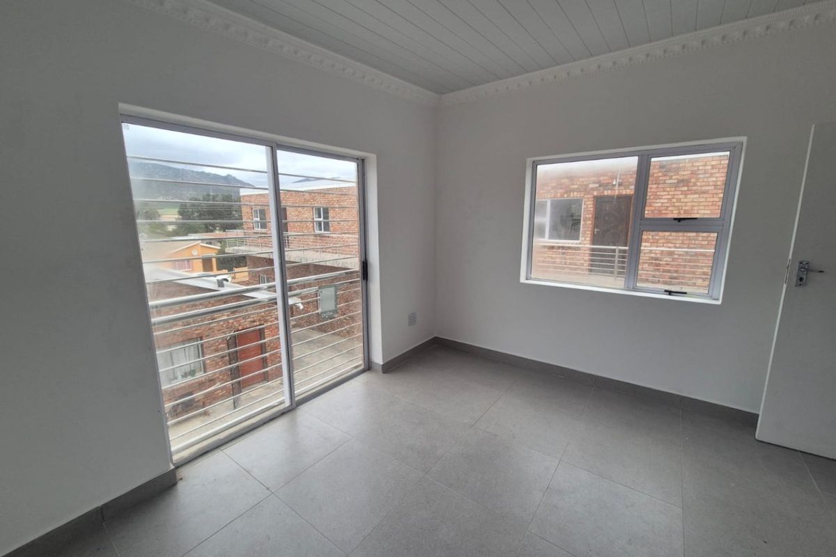 A bright, empty bedroom featuring tiled floors, a tongue and groove ceiling with decorative cornice, and large windows with security bars.