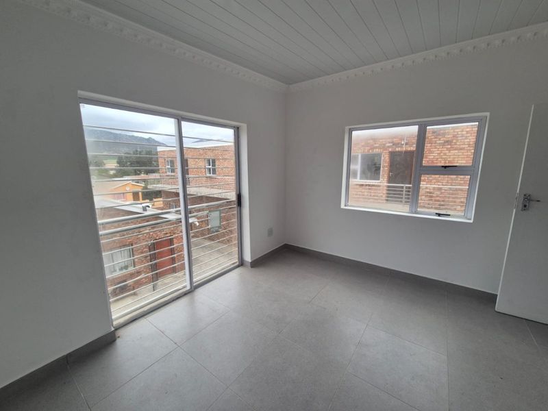A bright, empty bedroom featuring tiled floors, a tongue and groove ceiling with decorative cornice, and large windows with security bars.