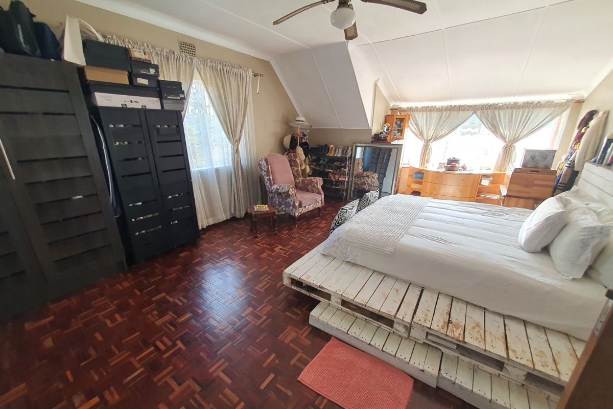 Spacious bedroom featuring classic parquet flooring, a ceiling fan, and a unique sloped ceiling design, offering a comfortable and functional living space.