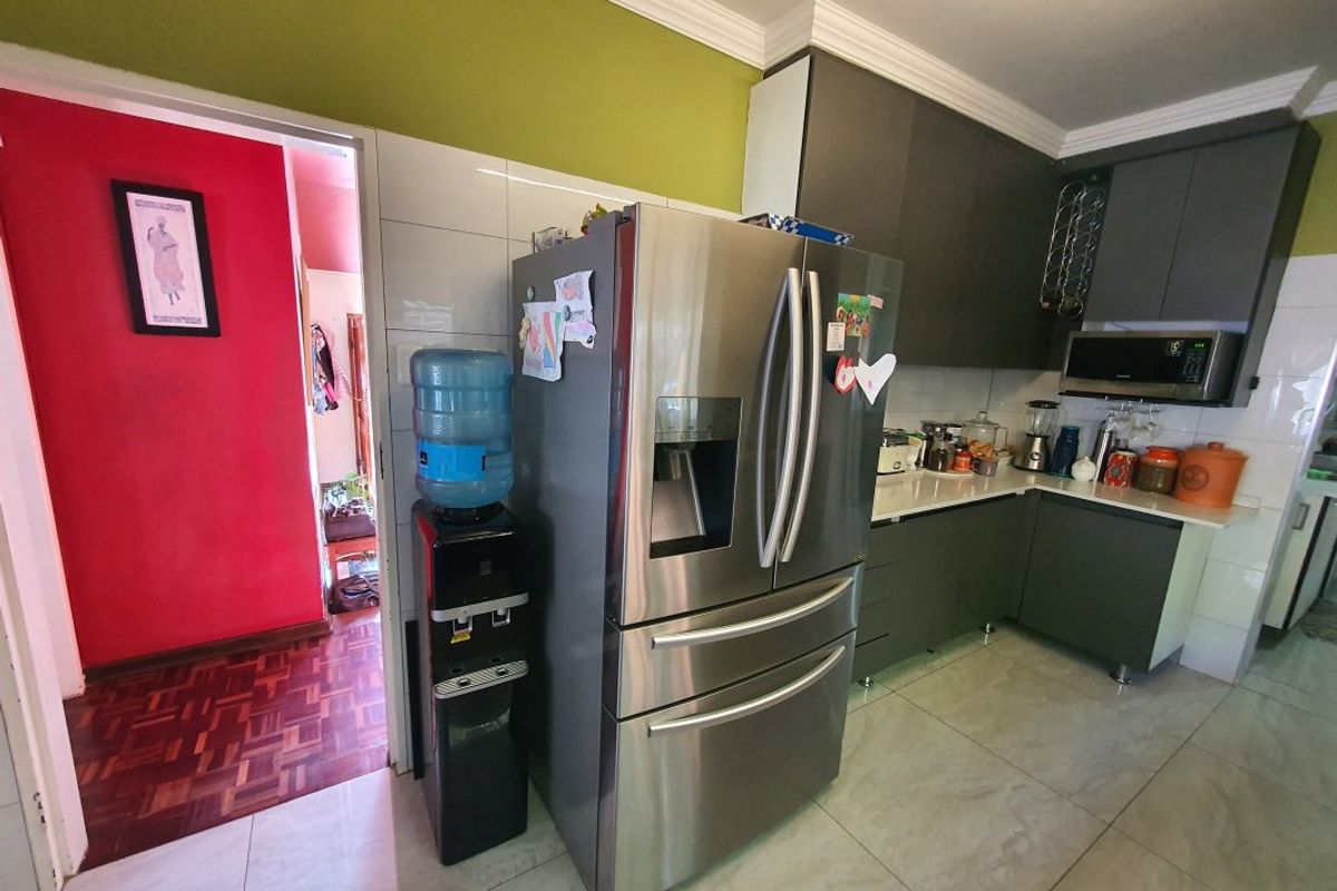 A functional kitchen featuring modern dark grey cabinetry, stone countertops, and a built-in microwave, complemented by neutral floor tiles and crown molding.