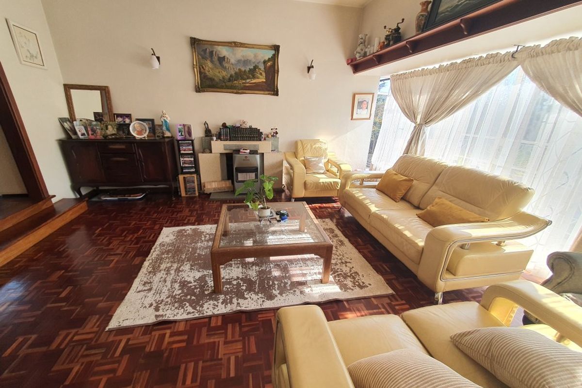 A spacious living room featuring classic parquet flooring, a built-in fireplace, and large windows that provide ample natural light.