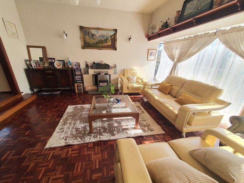 A spacious living room featuring classic parquet flooring, a built-in fireplace, and large windows that provide ample natural light.