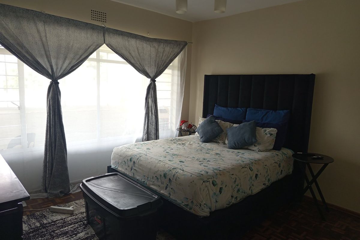 A bedroom featuring parquet flooring and a large window with natural light, providing a comfortable space for rest.