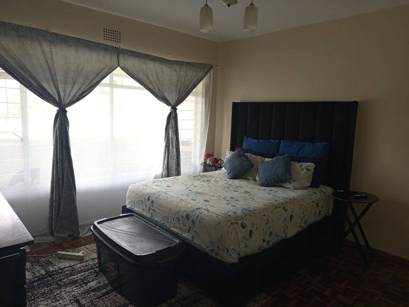 A bedroom featuring parquet flooring and a large window with natural light, providing a comfortable space for rest.