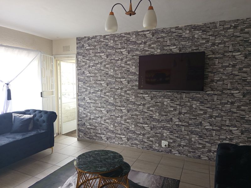 A living room featuring tiled flooring, a decorative stone-effect feature wall, and a security gate leading to an outdoor area.