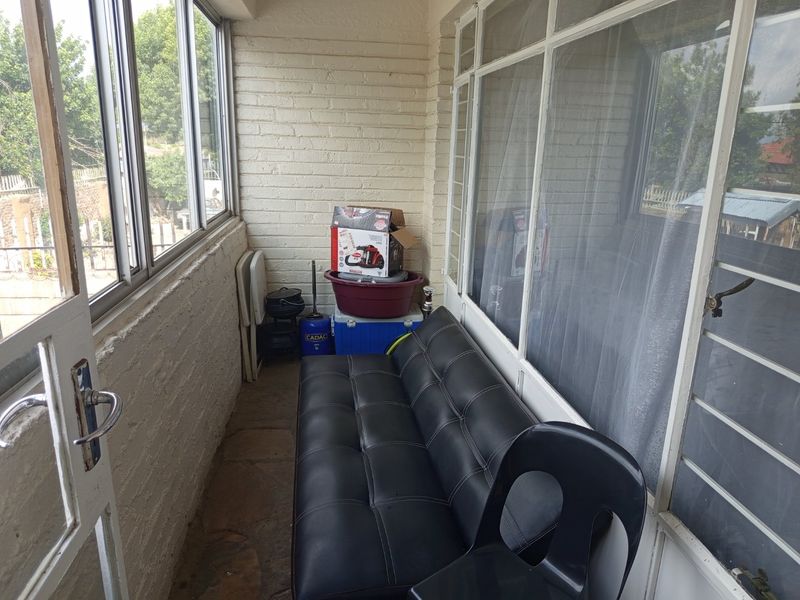 An enclosed balcony featuring painted brick walls, stone flooring, and large windows, offering a versatile space for relaxation or storage.