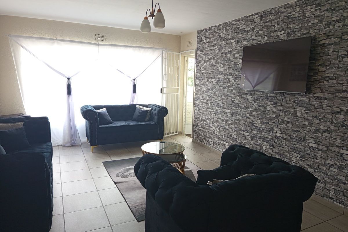 A living room featuring tiled flooring, a stone-effect feature wall, and access to an outdoor area through a security gate.