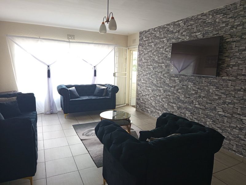 A living room featuring tiled flooring, a stone-effect feature wall, and access to an outdoor area through a security gate.