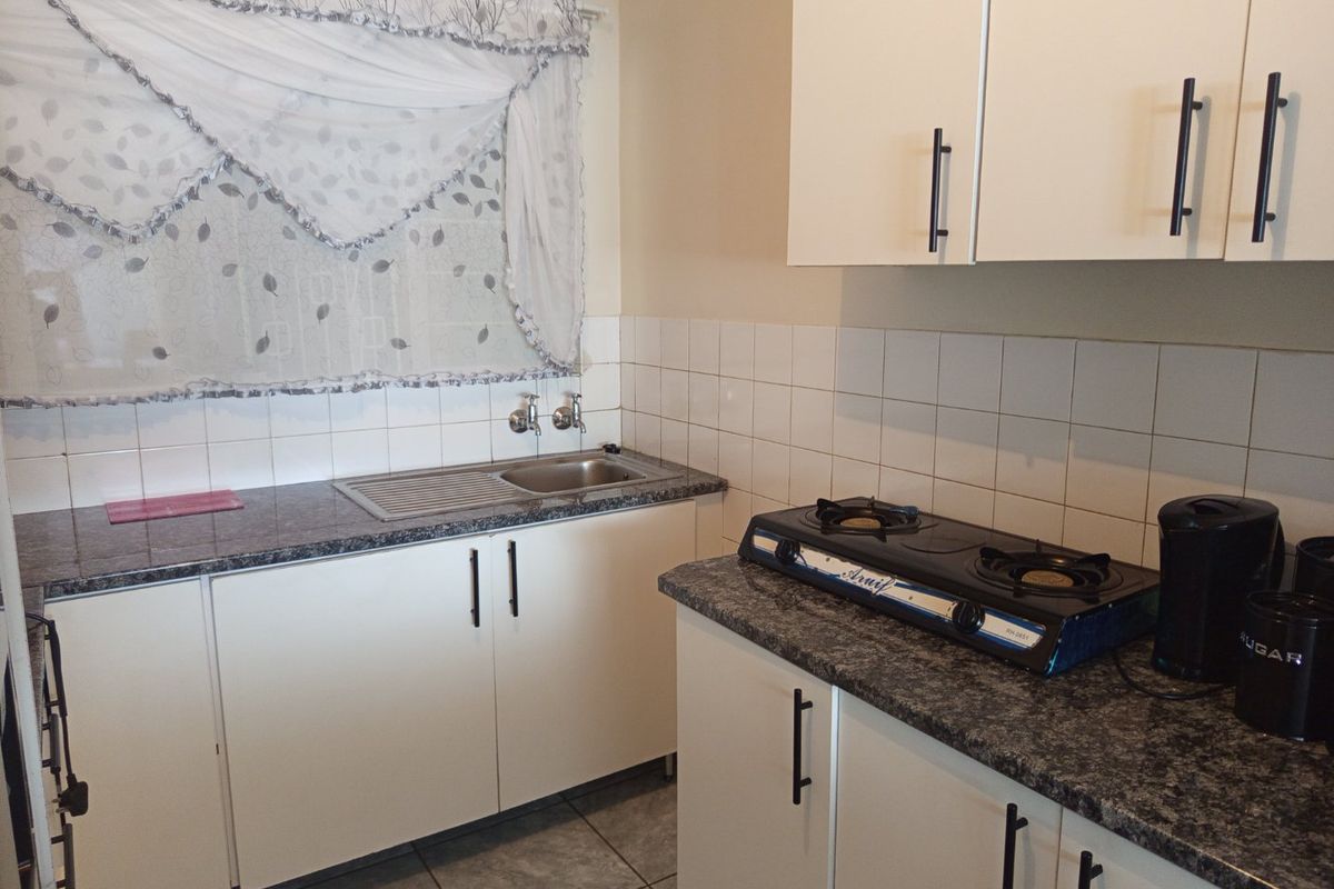 A functional kitchen featuring white cabinetry, granite-look laminate countertops, a stainless steel sink, and tiled backsplash.