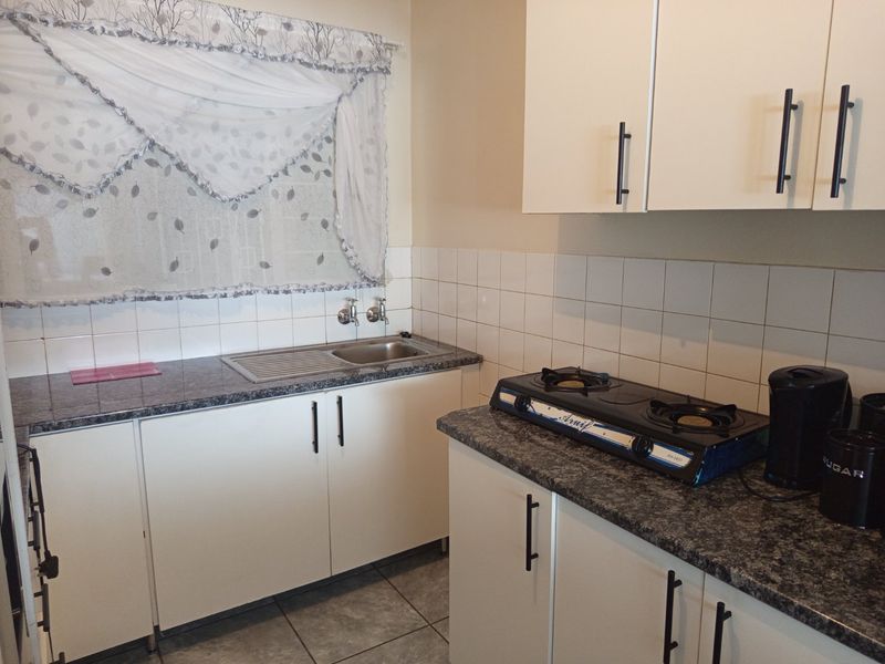 A functional kitchen featuring white cabinetry, granite-look laminate countertops, a stainless steel sink, and tiled backsplash.